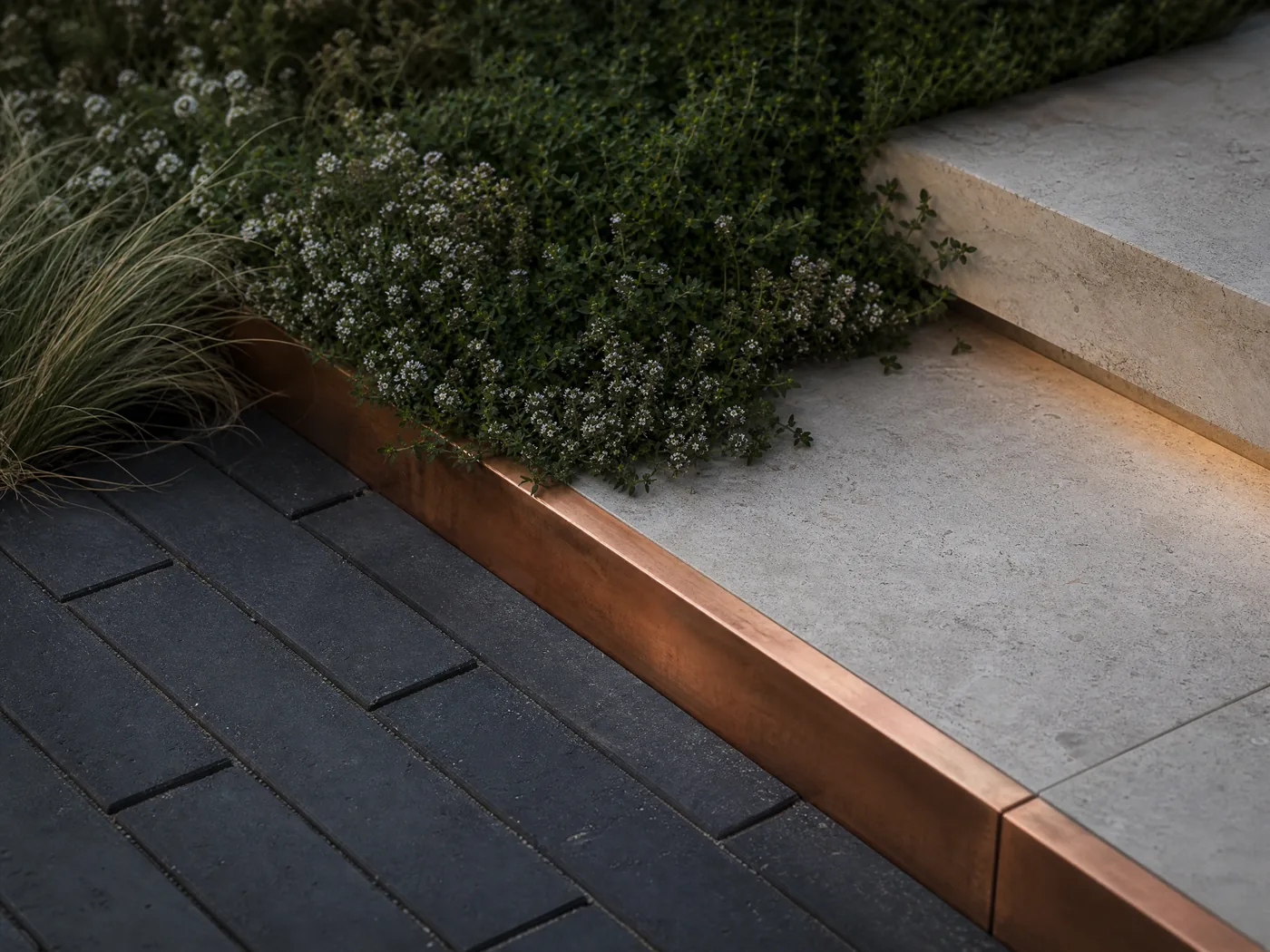 Landscape construction detail joining limestone, dark pavers, copper edging and soft planting